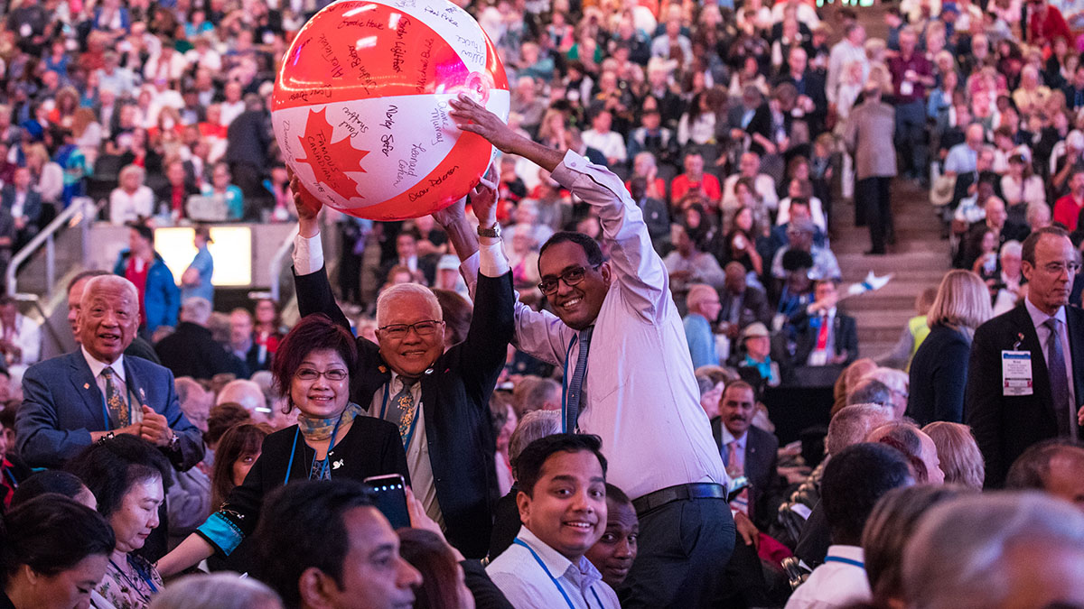 A group of convention attendees cheering and holding a beach ball that looks like the Canadian flag.