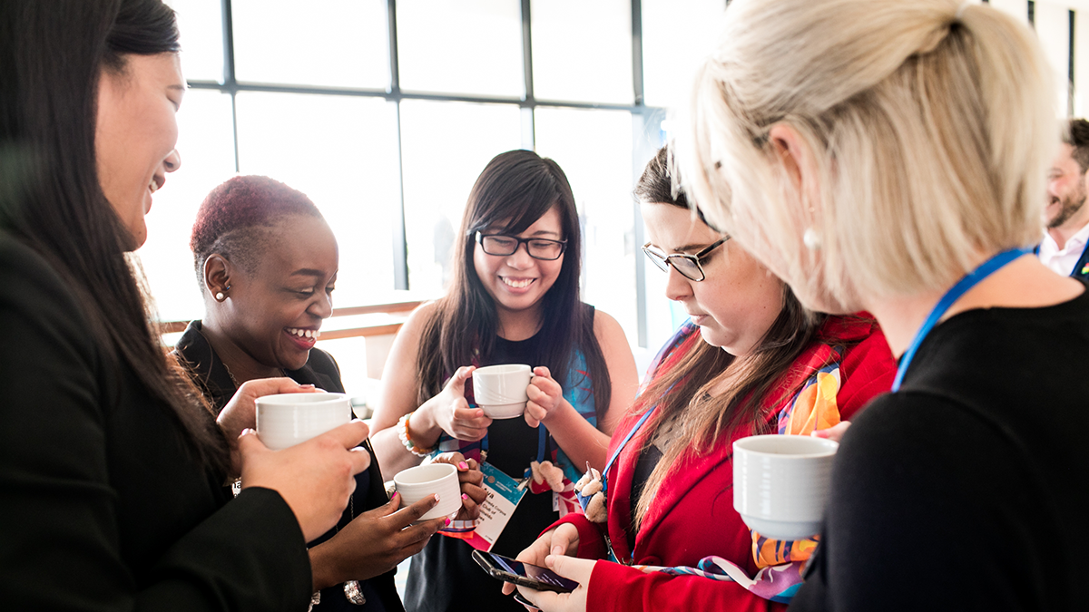 A group of people stand in a circle smiling and conversing. 